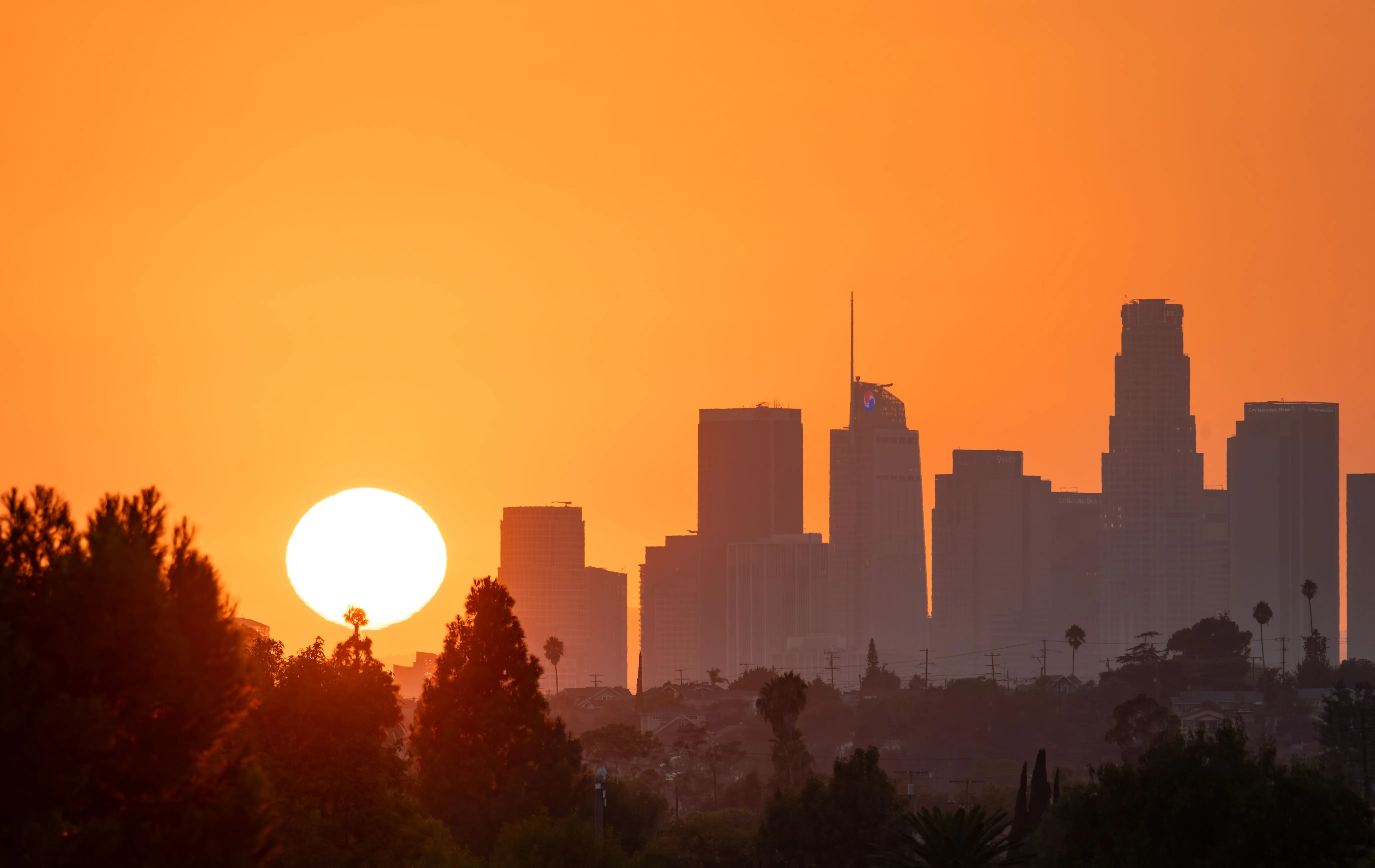 Tief stehende, glühende Sonne über einer dunstigen Stadt-Skyline
