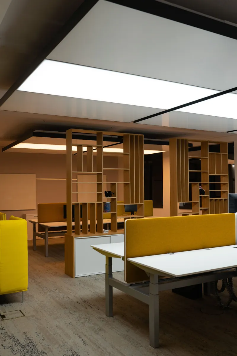 Lounge- und Arbeitsbereich der Sebastian Blum GmbH mit gelbem Sofa, Holzregal-Raumteiler und abgependelten interpanel Klimaleuchten