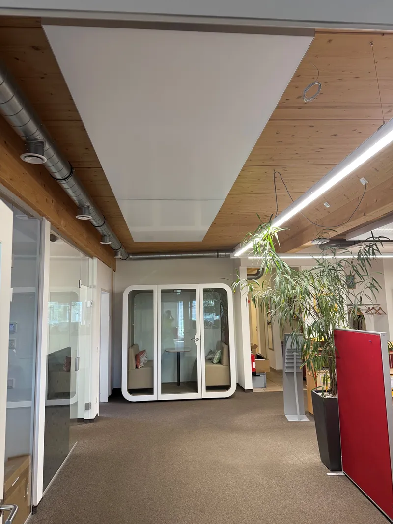 Offener Bereich bei SOTO mit einem weißen interpanel Deckensegel in der Holzdecke, verglaster Telefonbox und Pflanzen.
