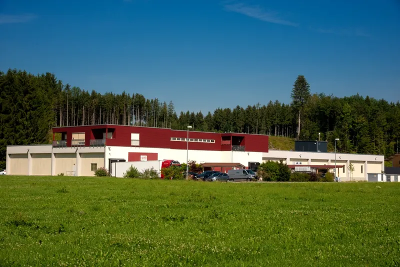 Betriebsgebäude von SOTO Bio-Spezialitäten in Bad Endorf mit rot-weißer Fassade und Flachdach vor Wald und Wiese.