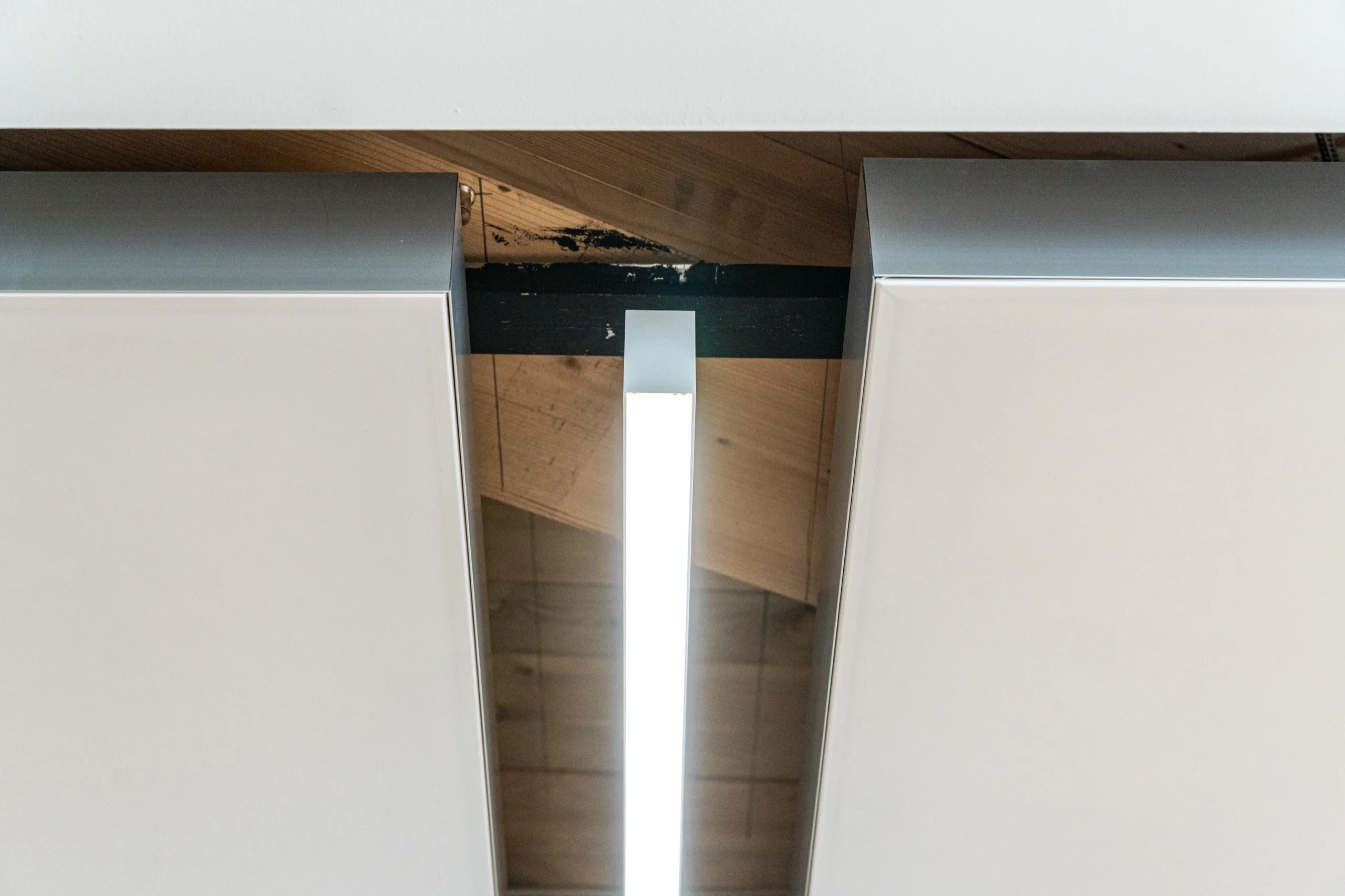 Kante zweier frei abgehängter interpanel Akustikleuchten mit sichtbarer Segeltiefe und schmaler Lichtfuge vor einer Holzdecke