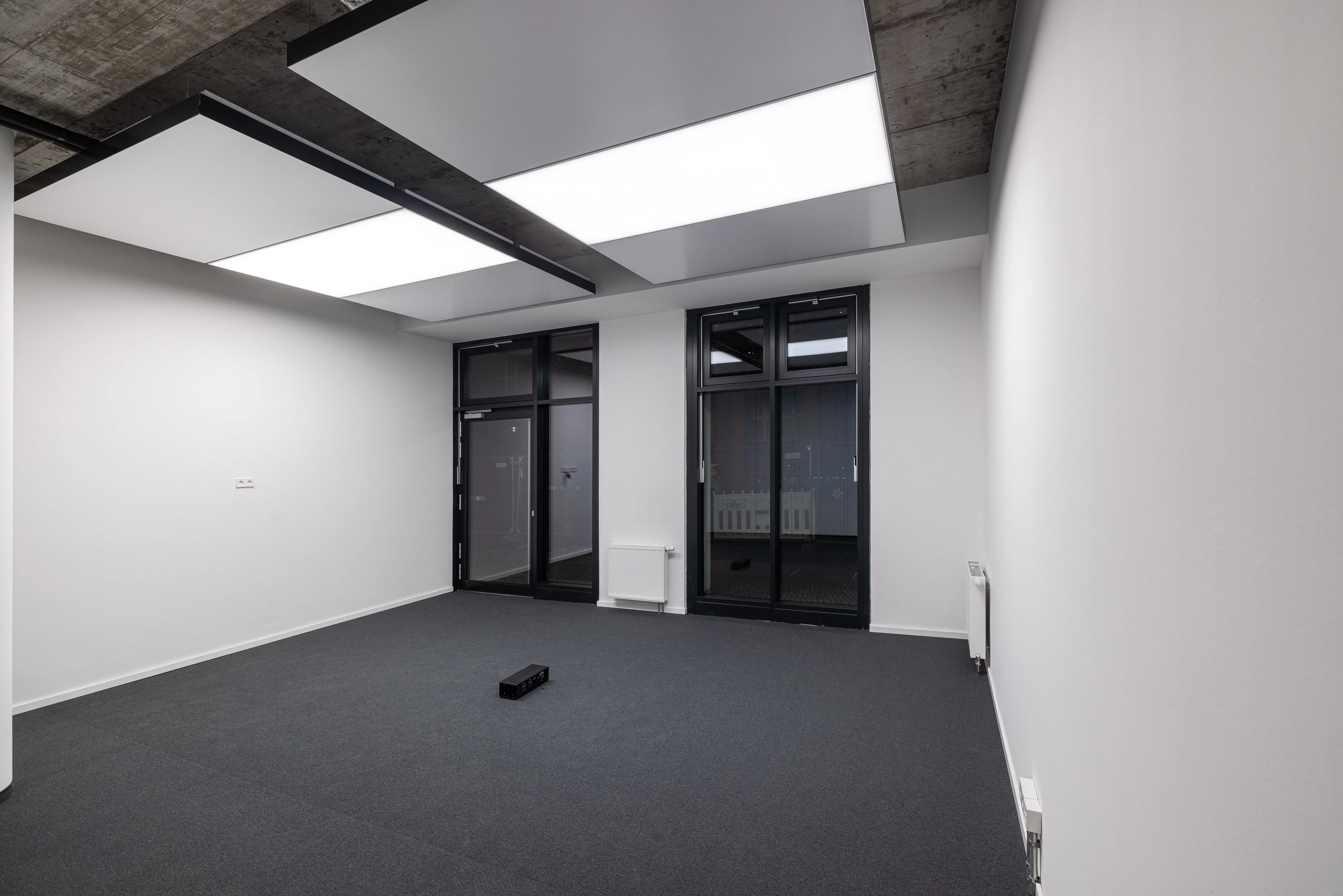 Zwei interpanel Deckensegel als leuchtende Kühlflächen in einem Büro mit Sichtbeton-Rohdecke