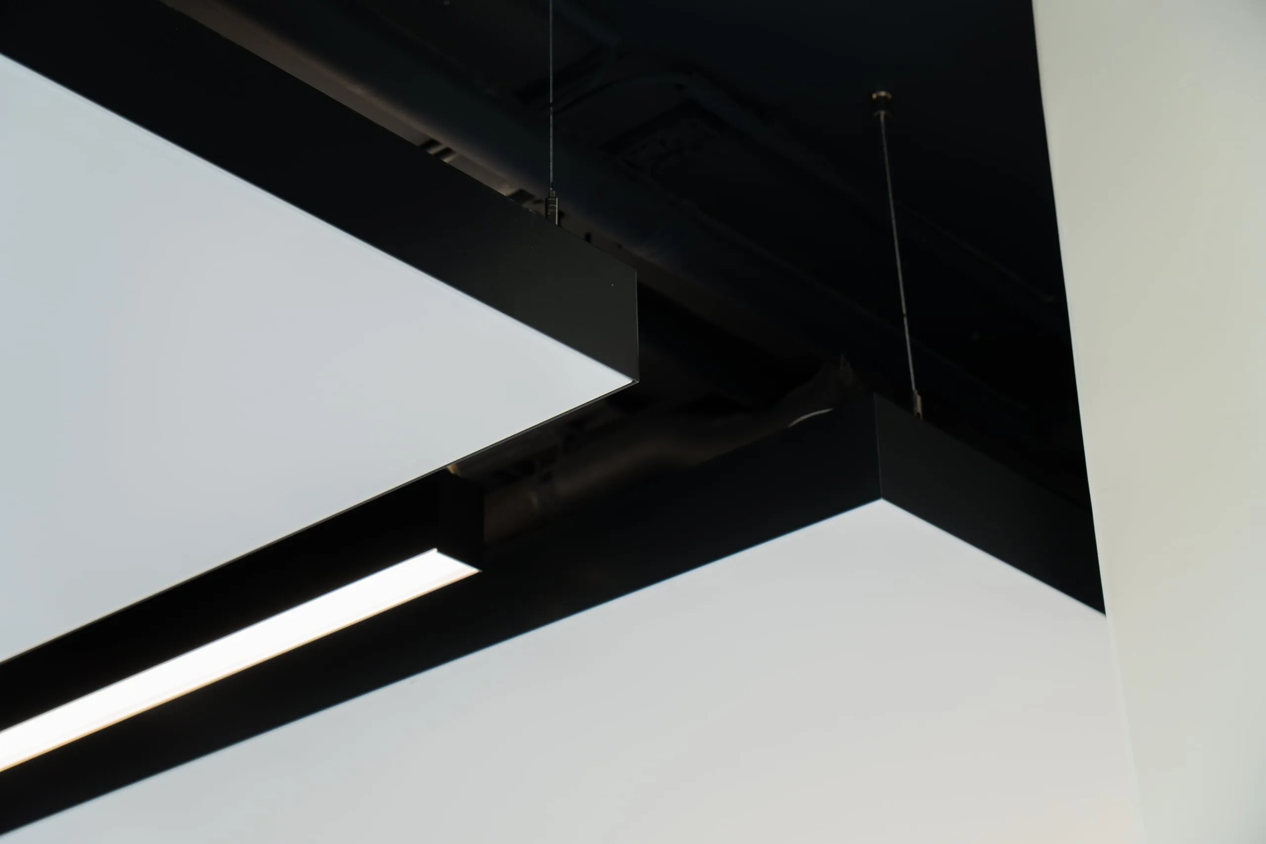 interpanel Deckensegel mit anthrazitfarbenem Rahmen und integriertem Linearlicht, Untersicht vor dunkler Industriedecke
