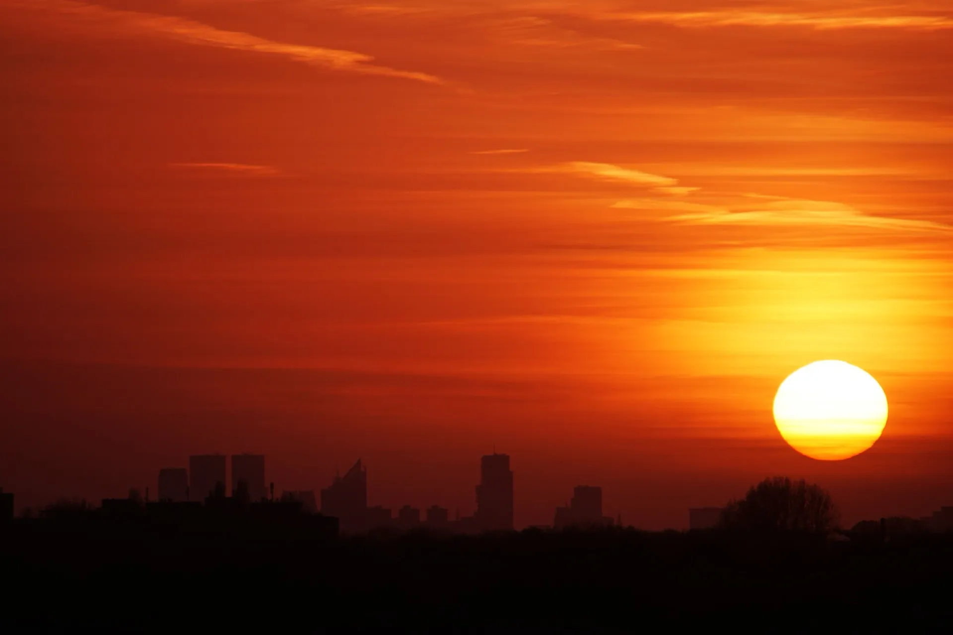 Glutrot untergehende Sonne über einer Stadtsilhouette an einem Hitzetag