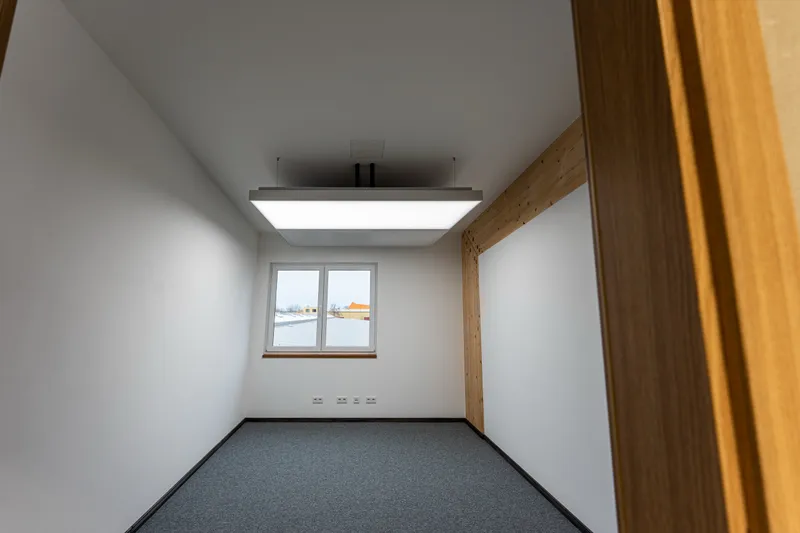 Büroraum im Holzbau mit zwei leuchtenden interpanel Klimaleuchten zwischen Holzstützen