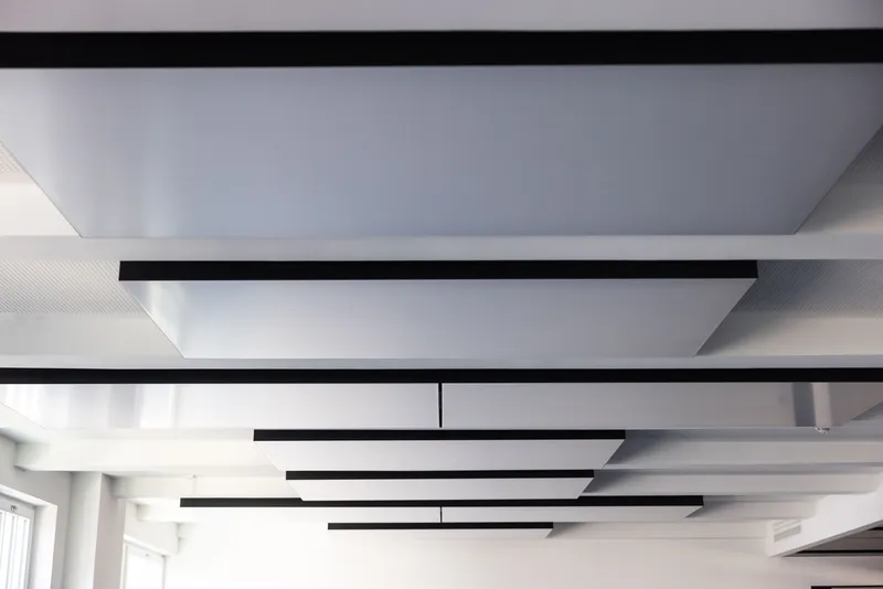 Detailansicht abgehängter interpanel Klimapanels mit schwarzer Seitenblende unterhalb der perforierten Akustikdecke der Kaisergalerie Hamburg.
