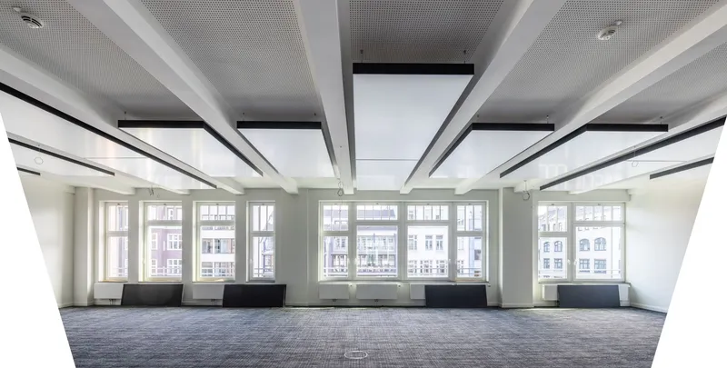 Leere Bürofläche der Kaisergalerie Hamburg mit reihenweise abgehängten interpanel Klimapanels zwischen weißen Deckenträgern, Fensterfront zum Innenhof und grauem Teppichboden.