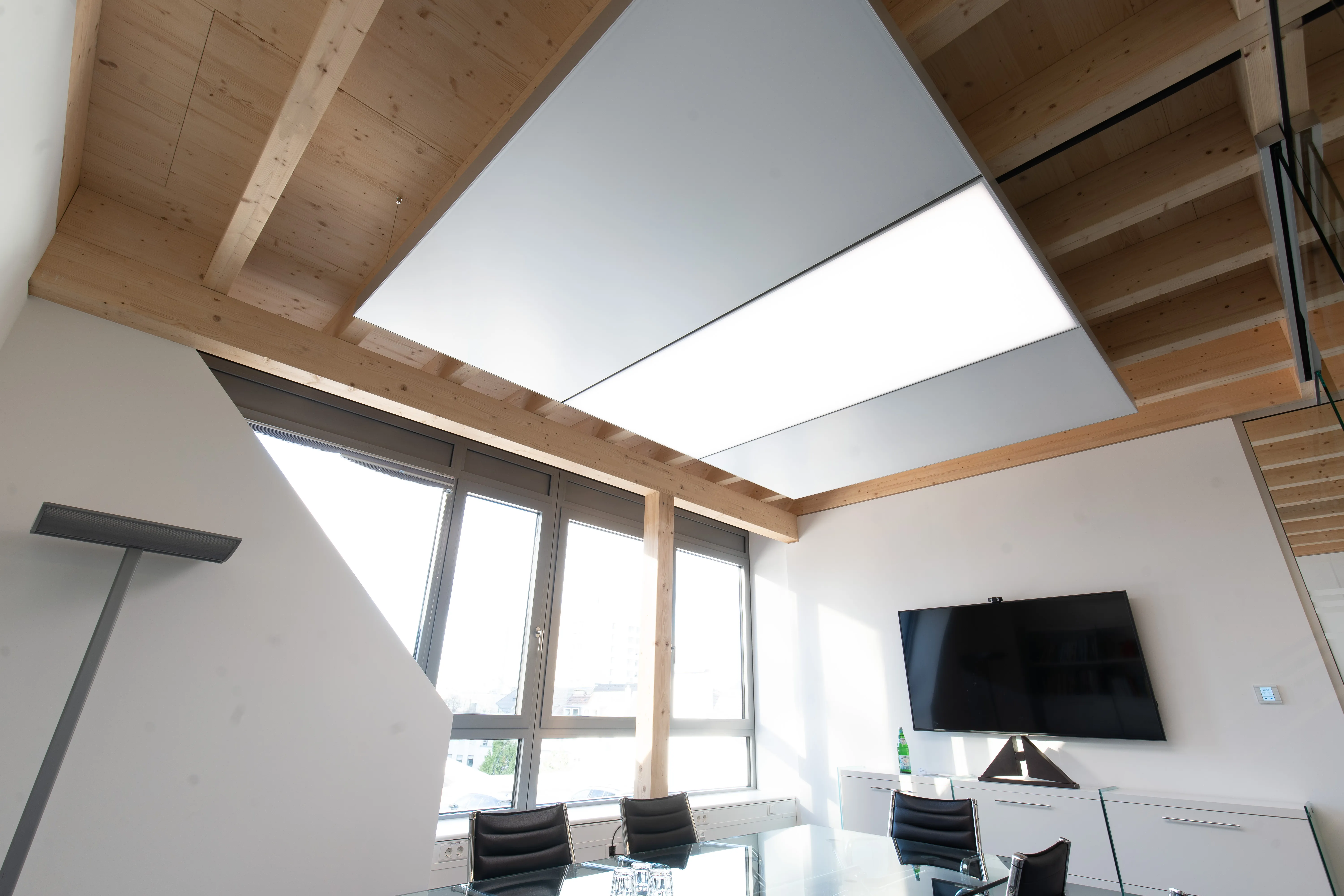 Große interpanel Klimaleuchte als leuchtende Fläche in einer Holzbalkendecke über einem Besprechungsraum mit Tageslicht